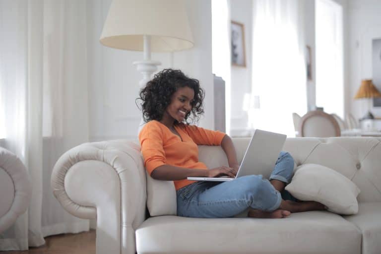 A woman in a virtual team sitting on a couch using a laptop.