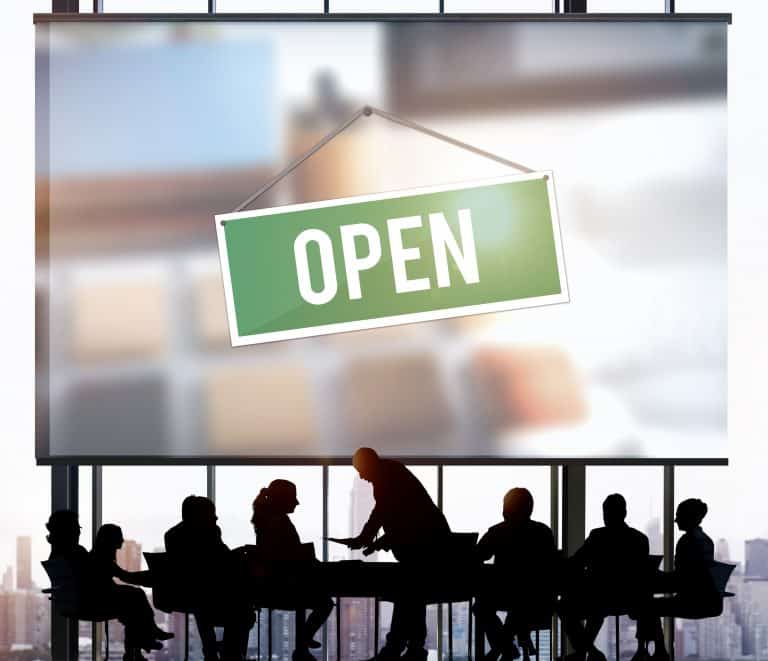 A group of people sitting around a table with an open sign in background.